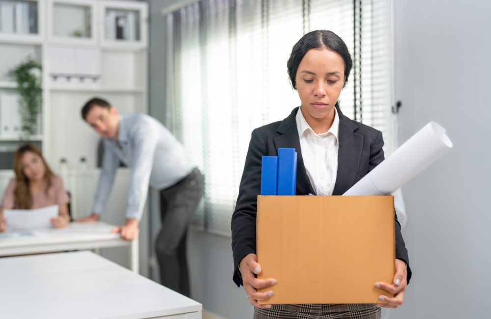 Woman office worker feel sad carrying cardboard boxes walking from office after resign, being fired or having employment contract expires.